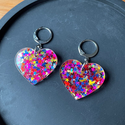 Petites boucles d'oreilles coeurs pendantes en acrylique avec des confettis étoiles et lunes multicolores